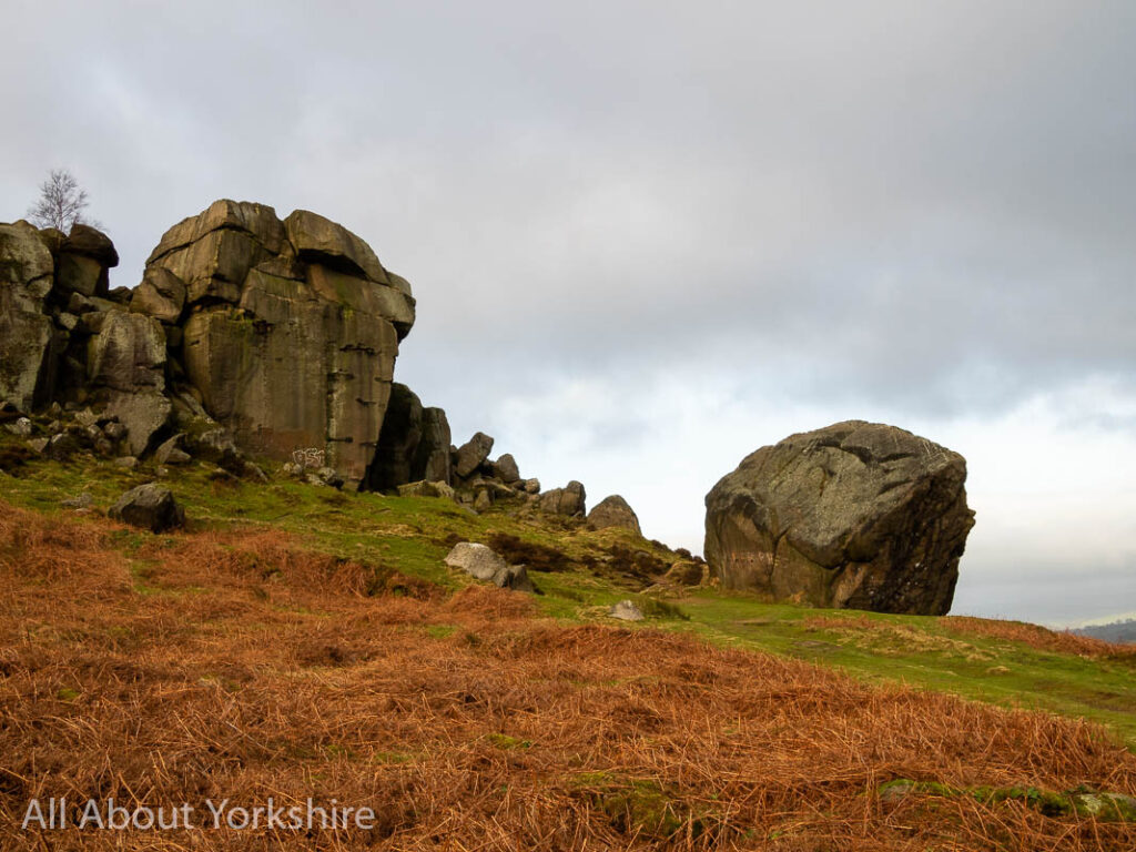 Open moorland in the foreground leading to a sandstone large rock formation in the midground called the Cow and Calf Rocks.