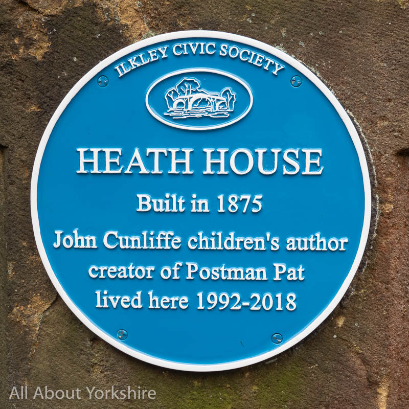 Blue plaque on stone wall. Plaque reads "Ilkley Civic Society, Heath House, Built in 1875, John Cunliffe children's author creator of Postman Pat lived here 1992-2018. 
