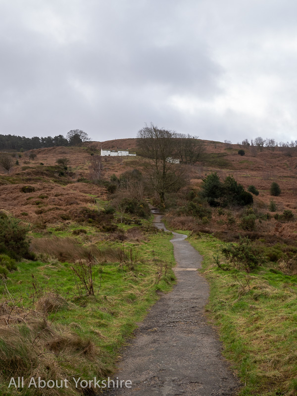 Tarmac path leading up through moorland to white buildings in the background that from White Wells on Ilkley moor